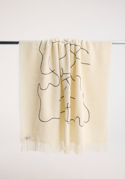 Tulip embroidered mohair blanket in off white, featuring a black continuous-line pattern, subtle fringe, and small fabric label, draped over a metal rod.
