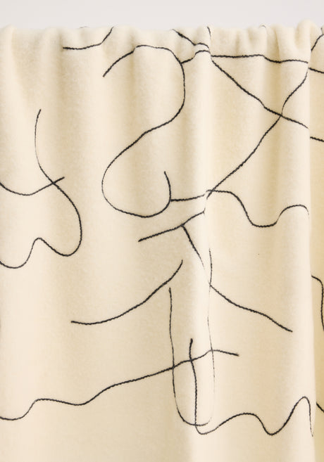 Tulip embroidered mohair blanket in off white, featuring a black continuous-line pattern, subtle fringe, and small fabric label, draped over a metal rod.