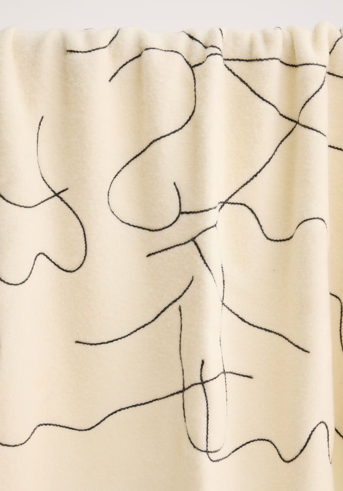 Tulip embroidered mohair blanket in off white, featuring a black continuous-line pattern, subtle fringe, and small fabric label, draped over a metal rod.