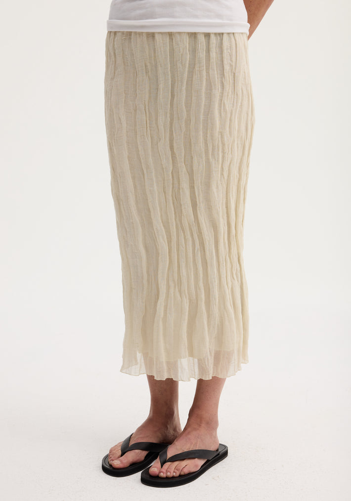 Textured tube skirt in cream, mid-calf length, with a crinkled finish. Paired with black slide flip-flops, showcasing its straight silhouette and elasticated waistband.