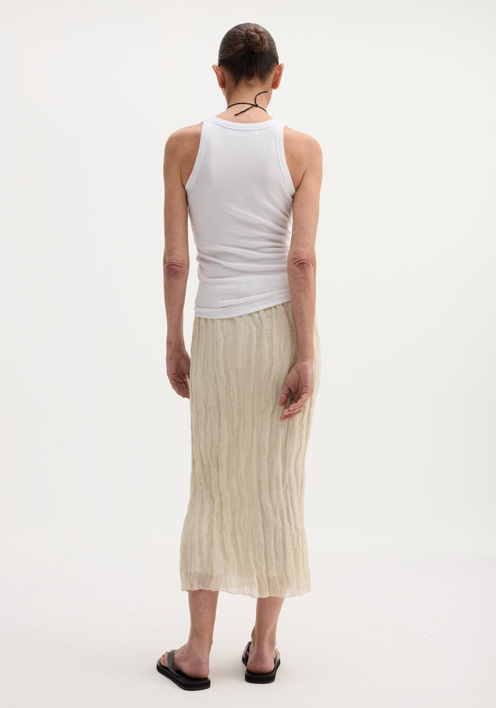 Person wearing a Textured tube skirt | cream, featuring a crinkled, mid-calf length with an elastic waistband, paired with a white tank top and black sandals.
