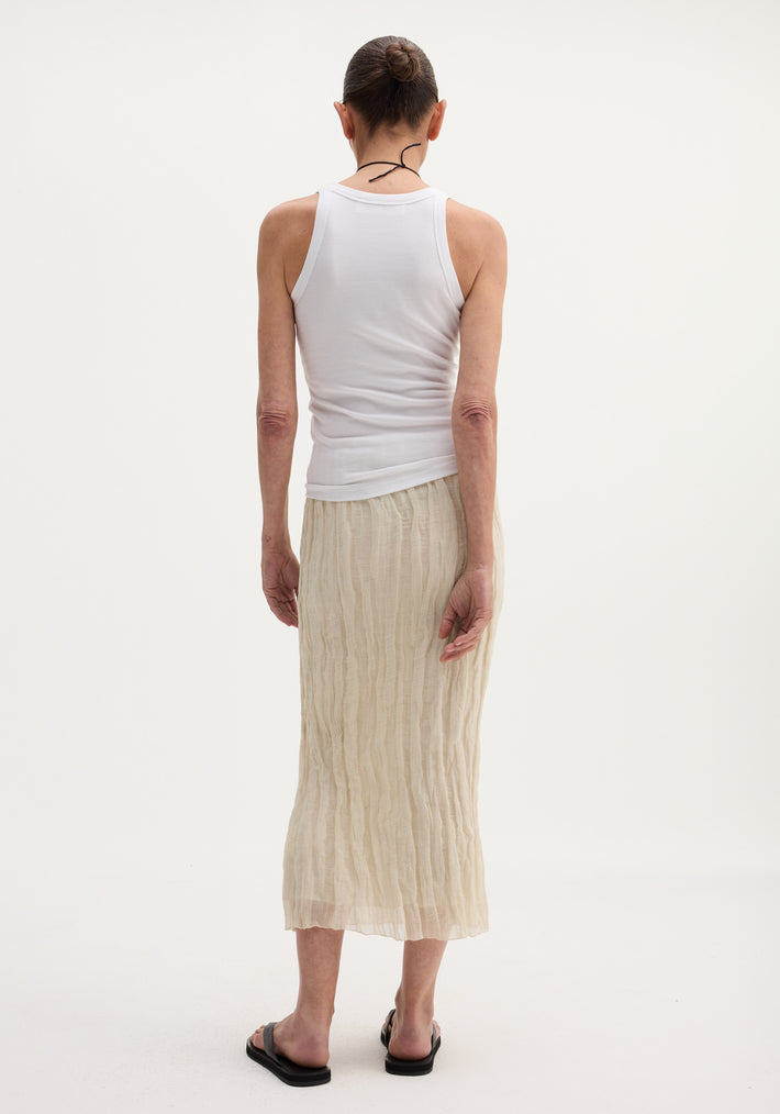 Person wearing a Textured tube skirt | cream, featuring a crinkled, mid-calf length with an elastic waistband, paired with a white tank top and black sandals.