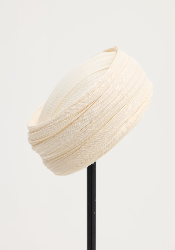 Sculptural silk hat in ivory, elegantly draped with finely pleated silk tulle, crafted by a Dutch artist, displayed on a slender black stand.
