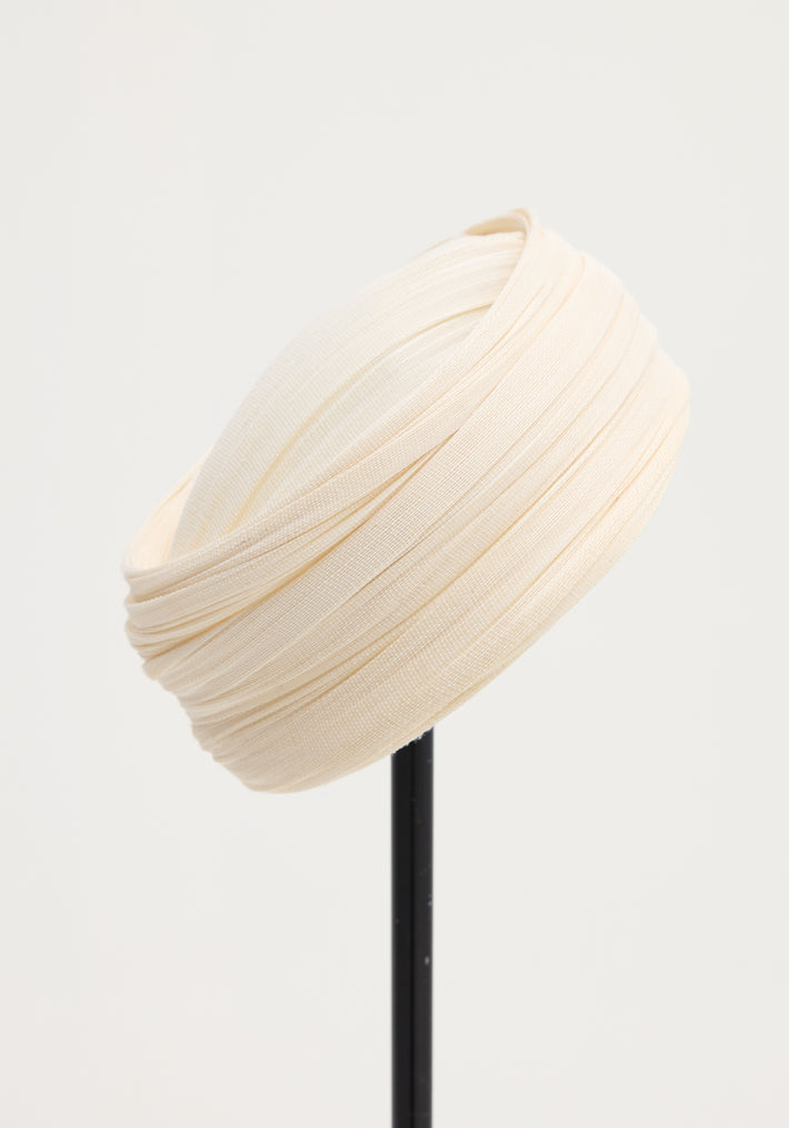 Sculptural silk hat in ivory, elegantly draped with finely pleated silk tulle, crafted by a Dutch artist, displayed on a slender black stand.