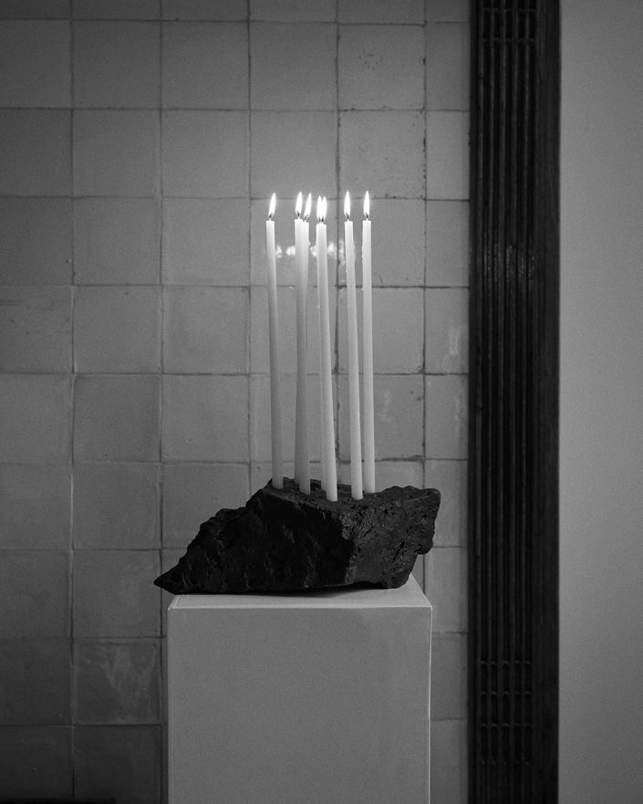 Sculptural Stone Candle Holder with seven lit taper candles on a white plinth, handcrafted from lava stone by Dutch artist Louis Crombag.