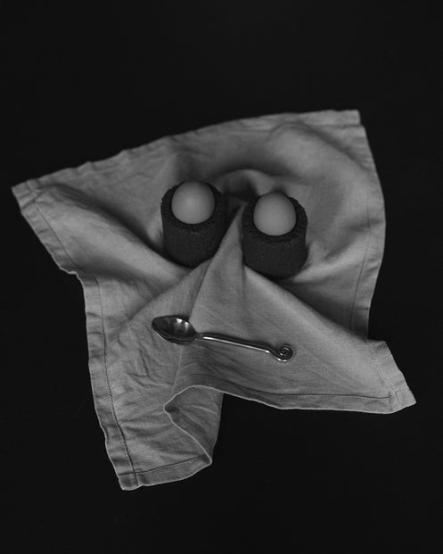 Egg Cups crafted from lava stone, shown in a minimalist setting with a linen napkin and teaspoon, highlighting their unique, handcrafted design.