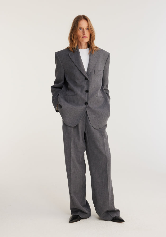 Person wears oversized blazer in grey melange with broad shoulders, styled with matching wide-leg trousers. Relaxed, androgynous tailoring from Frame's permanent collection.