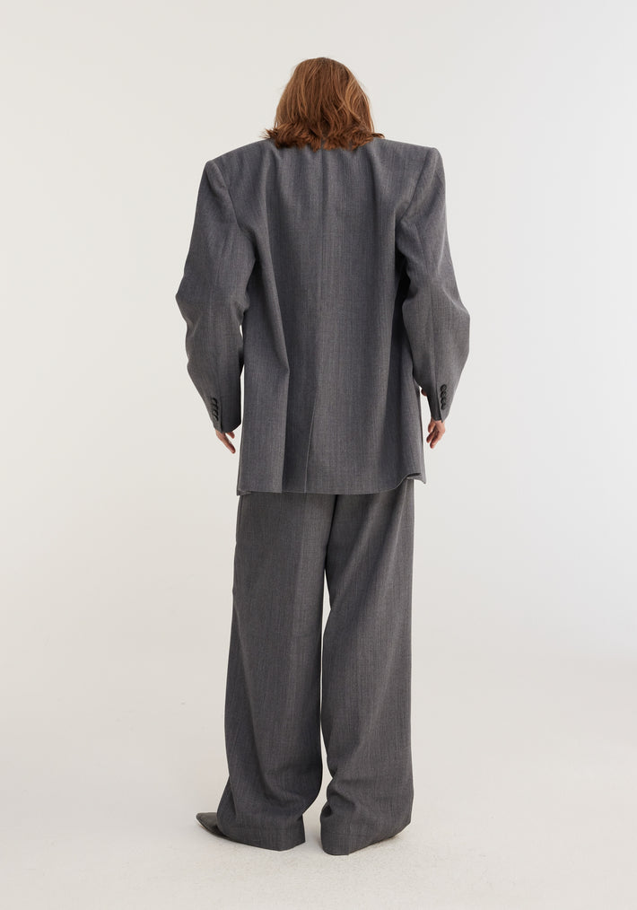 Person in a slate-gray melange oversized blazer with wide-leg trousers, showcasing a minimalist, androgynous style. Made from a Bisentino wool-blend fabric.