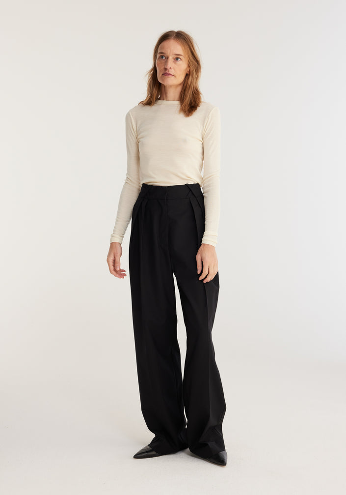 Fine merino long sleeve | off-white: Model in fitted cream merino wool top, long sleeves, crew neck, paired with high-waisted black trousers and pointed-toe shoes.