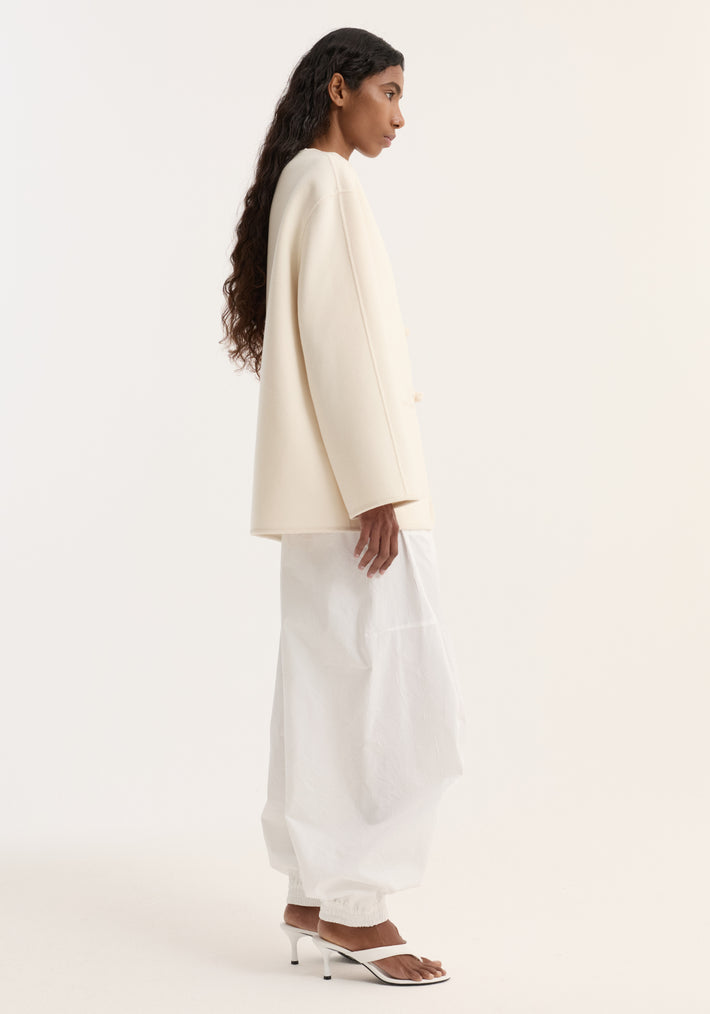 Model wearing a Double-faced wool pankou jacket with pankou knots, embroidered edges, and patch pockets, paired with voluminous trousers and low-heeled sandals.