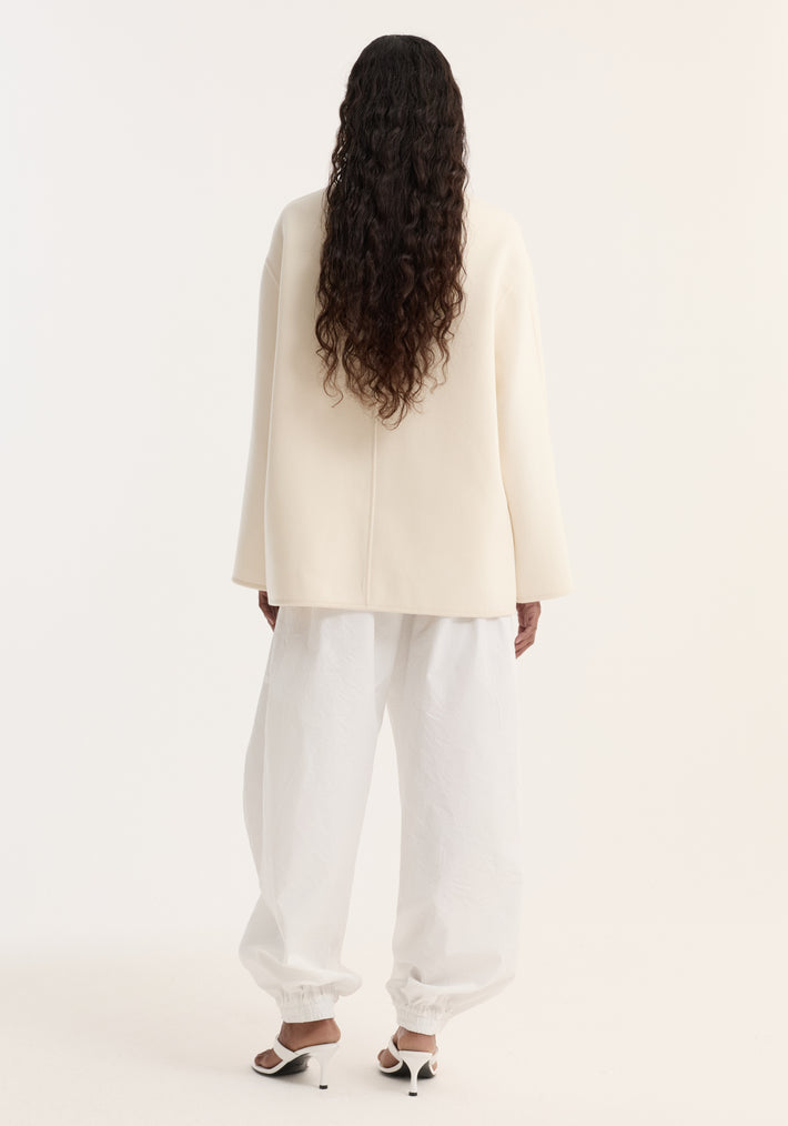 Back view of a person in a Double-faced wool pankou jacket with embroidered edges and patch pockets, paired with billowy trousers and open-back heeled sandals.