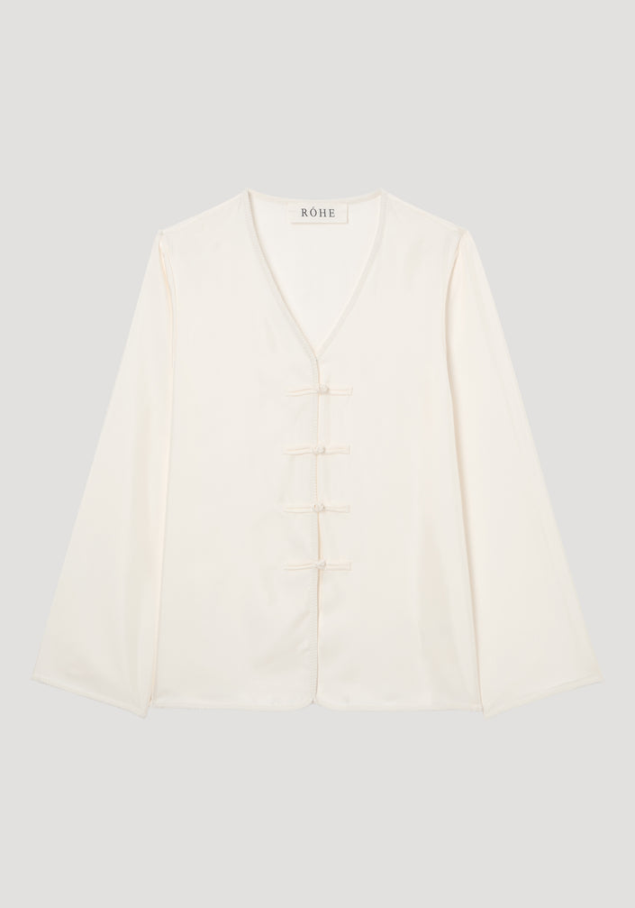 Mandarin silk top in cream with long sleeves, V-neck, embroidered edges, and four frog-style pankou closures, showcasing a relaxed fit ideal for layering.