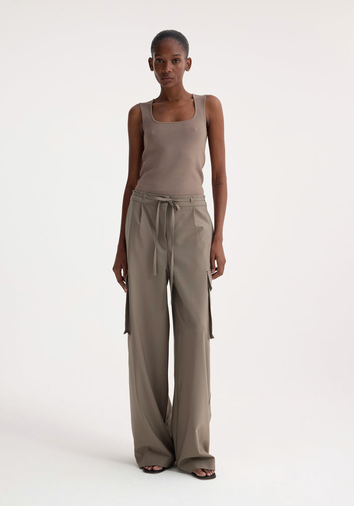 Woman wearing Bustier shaped knitted top in taupe, styled with high-waisted, wide-leg trousers and black sandals, standing in a fashion-forward pose.