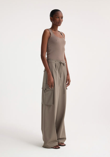 Woman wearing Bustier shaped knitted top in taupe, styled with high-waisted, wide-leg trousers and black sandals, standing in a fashion-forward pose.