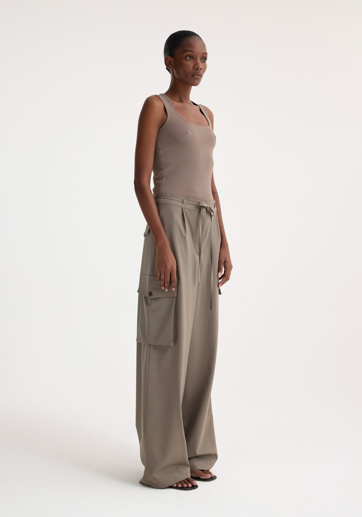 Woman wearing Bustier shaped knitted top in taupe, styled with high-waisted, wide-leg trousers and black sandals, standing in a fashion-forward pose.