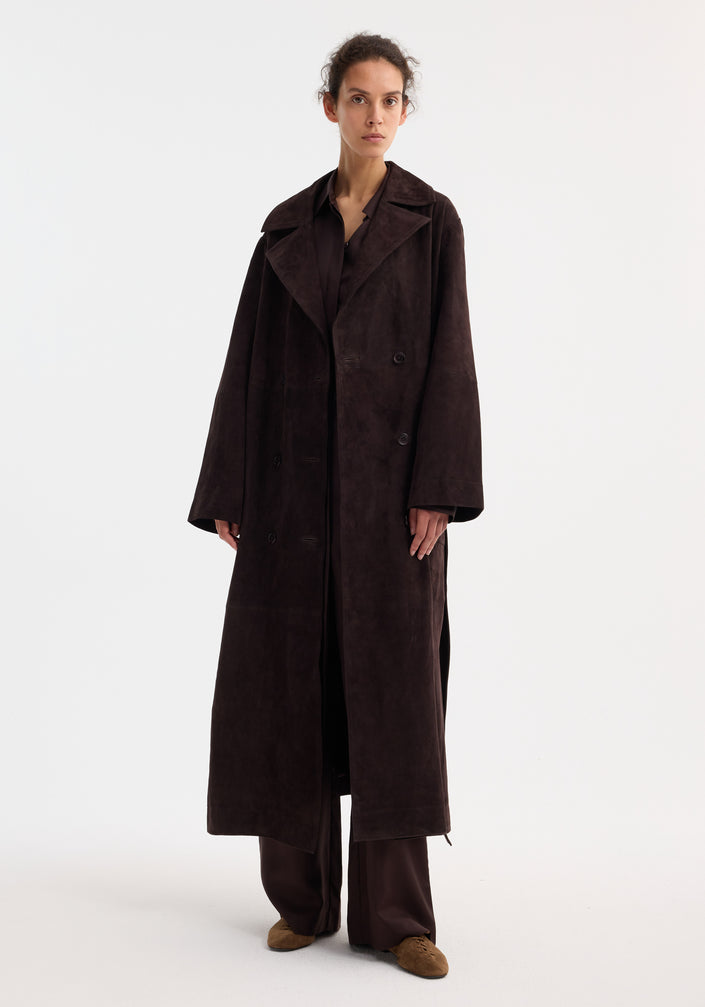 Model in a suede belted wrap coat, dark chocolate, with wide lapels and patch pockets, paired with matching trousers and light brown suede lace-up shoes.