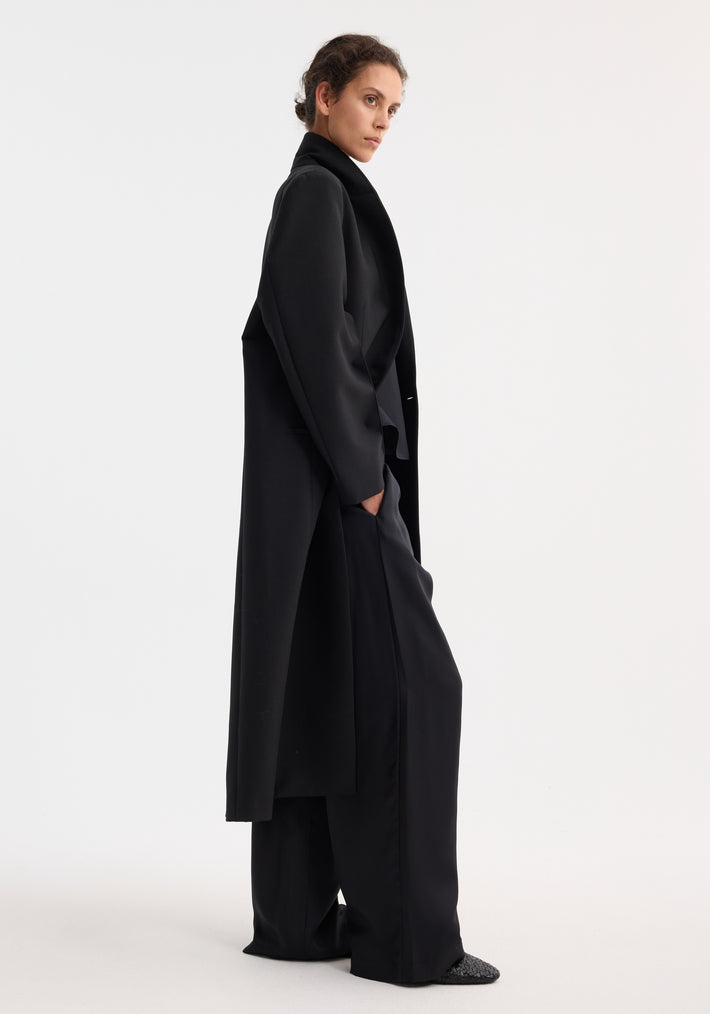 Signature opera coat in black, featuring a tailored fit, double-breasted lapels, and welt pockets. Paired with wide-leg trousers and low-profile shoes for a minimalist look.