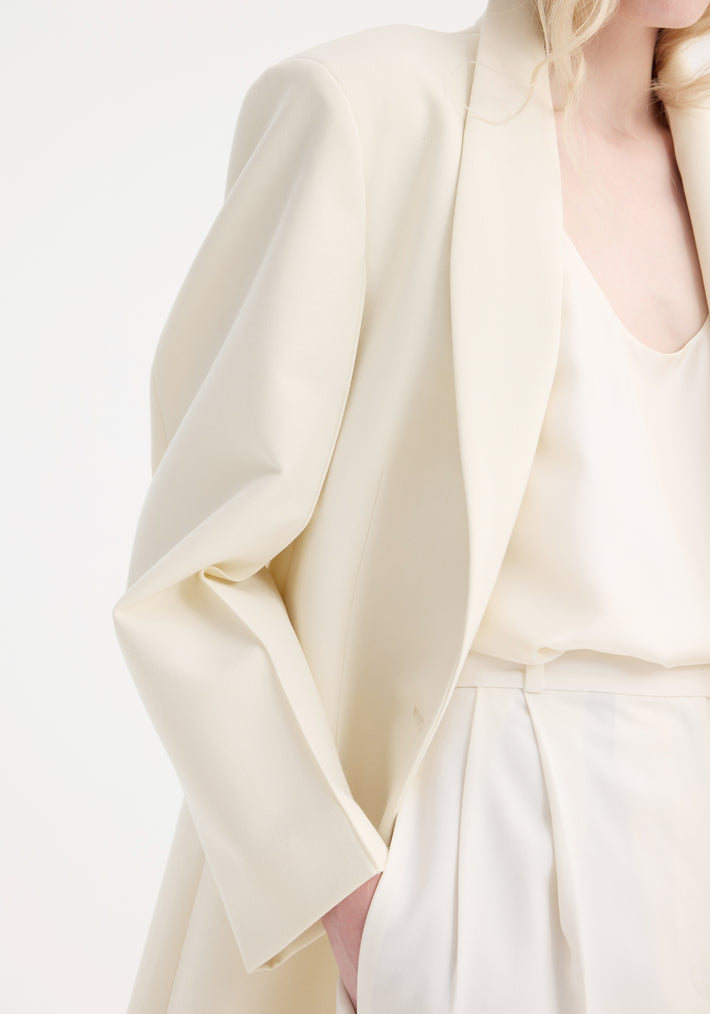 Close-up of a person in a cream blazer and trousers, illustrating the Signature opera coat's structured elegance and refined tailoring for sophisticated layering.
