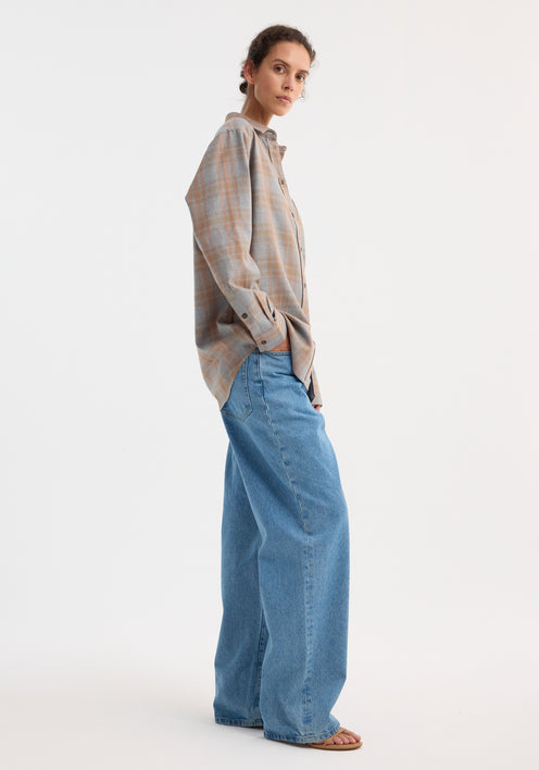 Model wearing an oversized Check shirt | powder check, with muted plaid pattern, paired with light-washed wide-leg jeans and tan slide sandals.