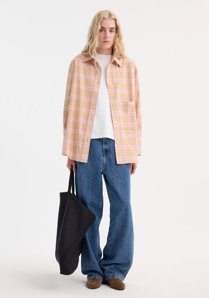 Person wearing Check flannel overshirt in pink beige check with relaxed fit, drop shoulders, over a white T-shirt, paired with wide-leg jeans and brown suede slip-ons.