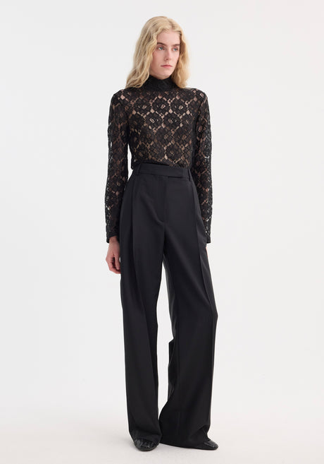 Light-haired person models the Lace turtleneck top | black, featuring a high-neck, long sleeves, and a fitted silhouette, paired with wide-leg trousers.