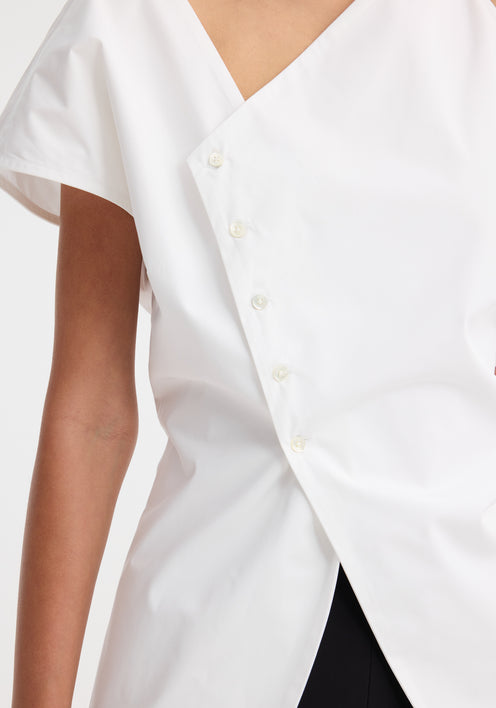Model in an Asymmetrical poplin top | optic white, featuring an angled hem, off-center buttons, and a side split, paired with black trousers and heeled sandals.