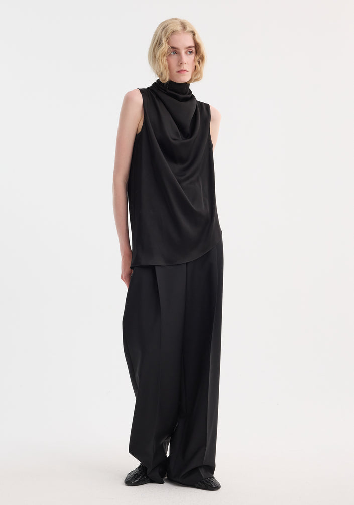 Model in a sleeveless draped satin top with a cowl neckline and wide-leg trousers, showcasing a minimalist, fluid silhouette.
