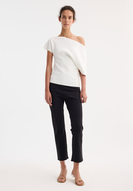 Model wearing Asymmetrical Punto Milano knitted top with slashed neckline and bell sleeve, paired with slim-fit black trousers and tan sandals, hair in updo.