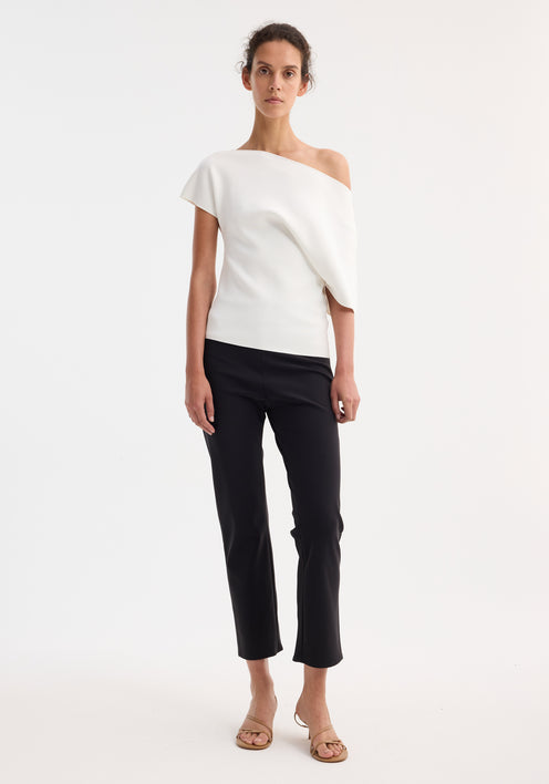 Model wearing Asymmetrical Punto Milano knitted top with slashed neckline and bell sleeve, paired with slim-fit black trousers and tan sandals, hair in updo.