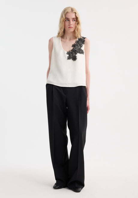 Slim woman in a Scoop-neck silk lace top with intricate black floral lace on shoulder, paired with high-waisted trousers. Perfect for minimalist wardrobes.