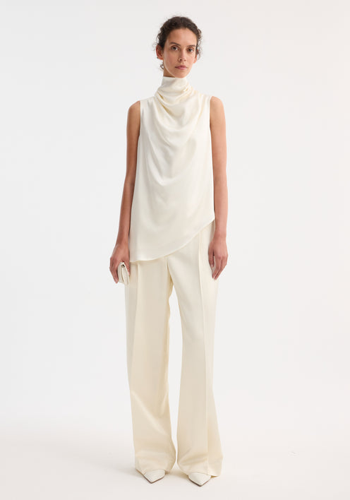 Model wearing Sleeveless draped satin top with cowl neckline, paired with high-waisted trousers and holding a clutch, showcasing minimalist, elegant style.