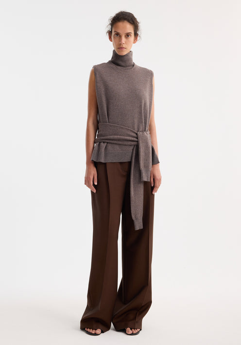 Model wearing Double-layered knit top | mud melange, featuring a sleeveless turtleneck layer and draped sweater, paired with wide-leg trousers and open-toe sandals.