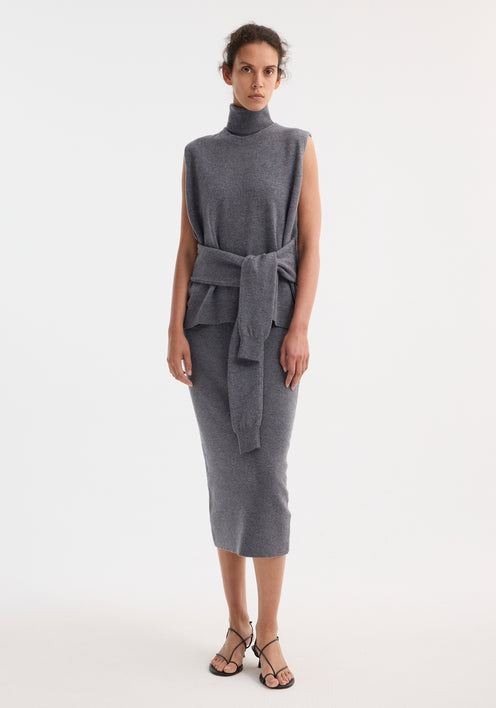 Model wears Double-layered knit dress in mid grey melange, featuring a sleeveless turtleneck top, matching midi skirt, and sweater tied around waist, with strappy sandals.