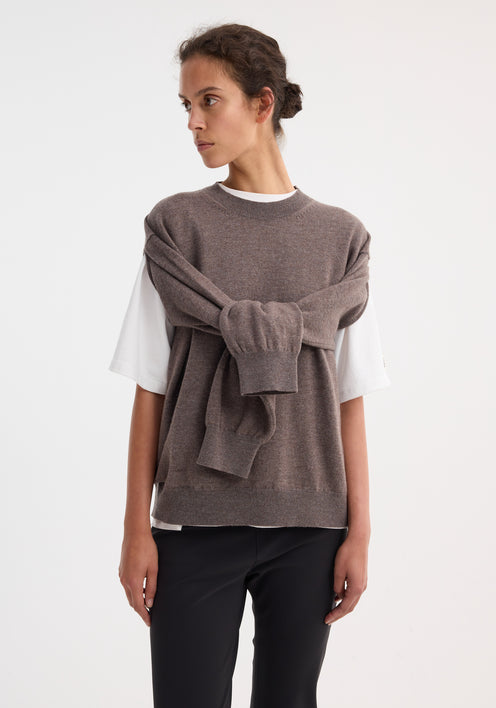 Model in Crew-neck with open armhole | mud melange vest over a white T-shirt, black trousers, and sandals, showcasing a versatile knit layering style.