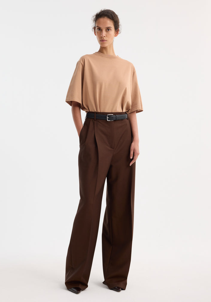 Mid-waist tailored trousers | mahogany, featuring a wide leg, tailored waistband, and double pleats, worn with a loose-fit tan T-shirt and black belt.