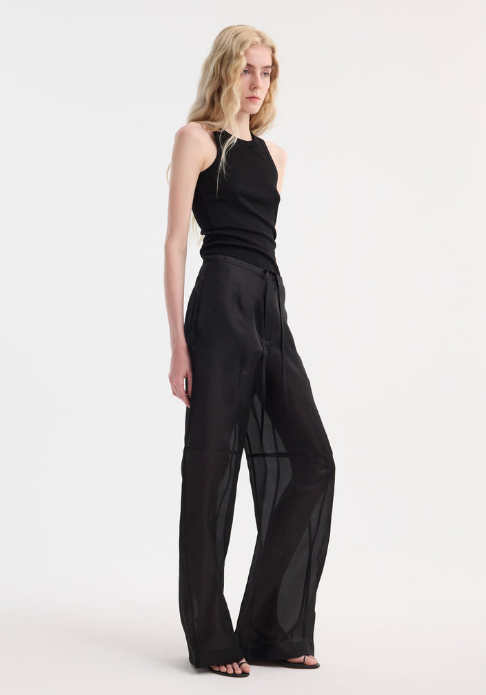 Model in Organza silk parachute trousers, showcasing wide-leg, semi-sheer flow and drawstring waist, paired with black tank top and strappy sandals.