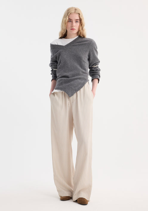 Young adult wearing wide leg silk trousers | classic stripe, featuring an elastic waistband and drawstring, paired with a charcoal-gray sweater over a white T-shirt.