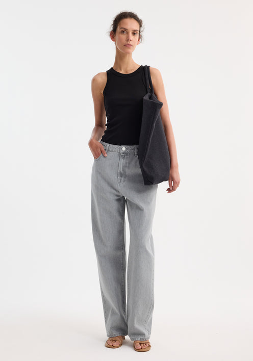 Person wearing Signature baggy fit denim in washed grey, featuring low-waist, wide-leg fit. Paired with a black tank top, tote bag, and tan sandals.