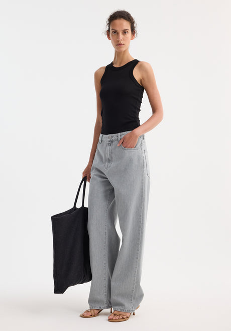 Person wearing Signature baggy fit denim in washed grey, featuring low-waist, wide-leg fit. Paired with a black tank top, tote bag, and tan sandals.