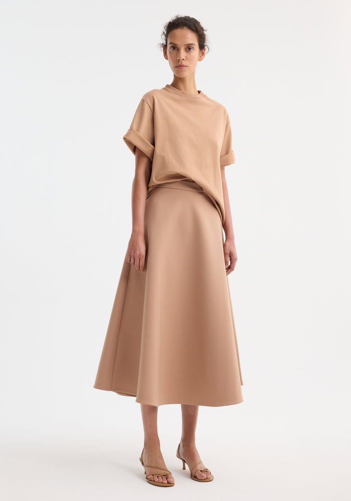 Model wearing A-line skirt | powder, showcasing a high-waisted, ankle-length cut with side pockets, paired with a matching oversized T-shirt and beige sandals.