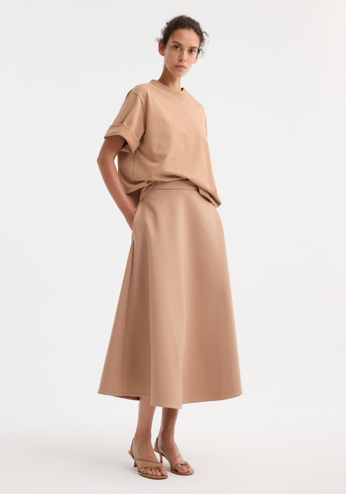 Model wearing A-line skirt | powder, showcasing a high-waisted, ankle-length cut with side pockets, paired with a matching oversized T-shirt and beige sandals.