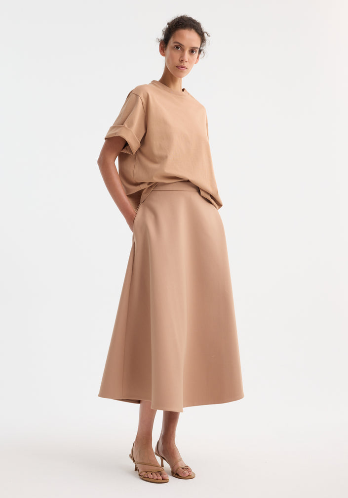 Model wearing A-line skirt | powder, showcasing a high-waisted, ankle-length cut with side pockets, paired with a matching oversized T-shirt and beige sandals.