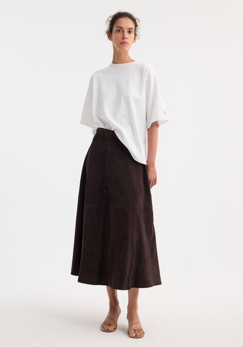 A-line suede skirt in dark chocolate, featuring a soft, voluminous shape. Model pairs it with a white T-shirt and tan sandals for a minimalist look.