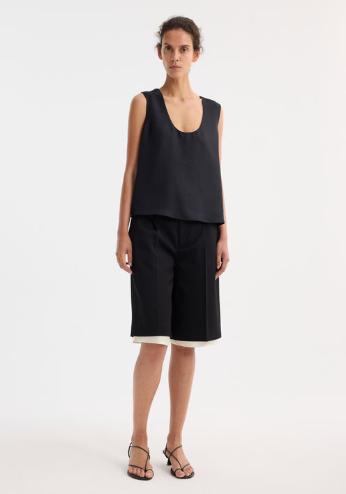 Model wearing Contrast extended lining shorts in black, featuring sharp pleats and a tailored waistband, paired with a loose sleeveless top and heeled sandals.
