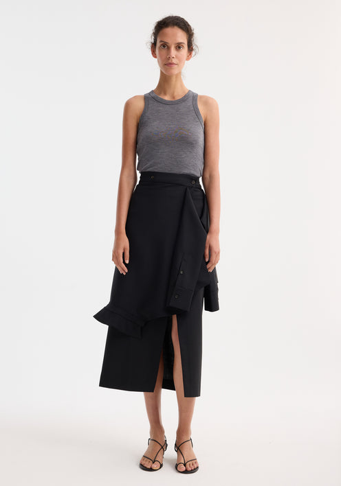 Woman wearing a black Shirt wrap skirt with asymmetrical hem and waist tie sleeve detail, paired with a gray tank top and black sandals.