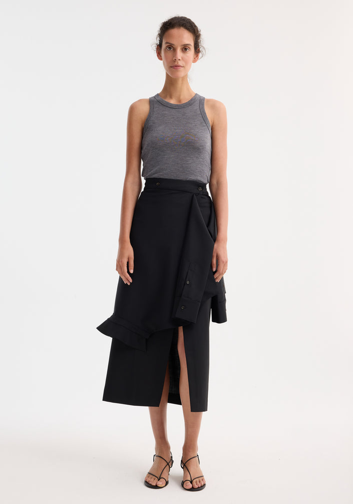 Woman wearing a black Shirt wrap skirt with asymmetrical hem and waist tie sleeve detail, paired with a gray tank top and black sandals.