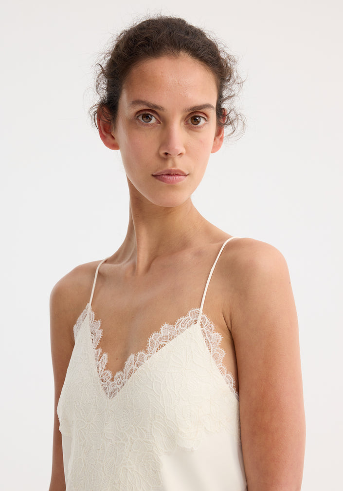 Model wearing Lace slipdress | cream, featuring a full-length design with lace-trimmed V-neck, ultra-thin spaghetti straps, and flowing silhouette, paired with tan sandals.