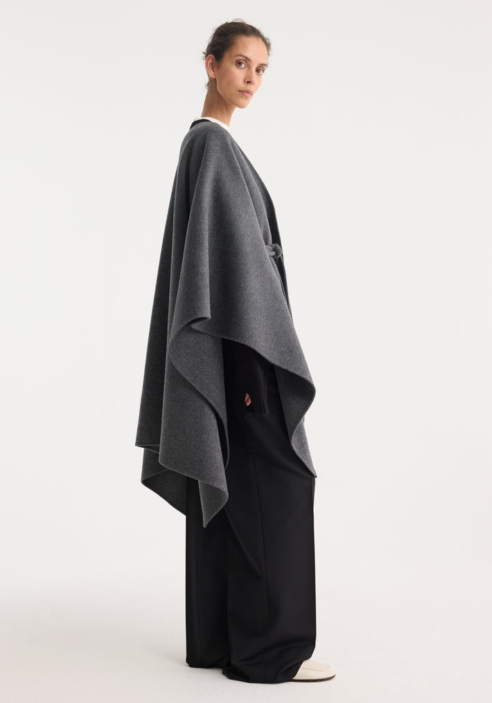 Double-faced belted poncho in mid grey melange, showcasing a cape silhouette with a soft drape, worn by a model with black wide-leg trousers.