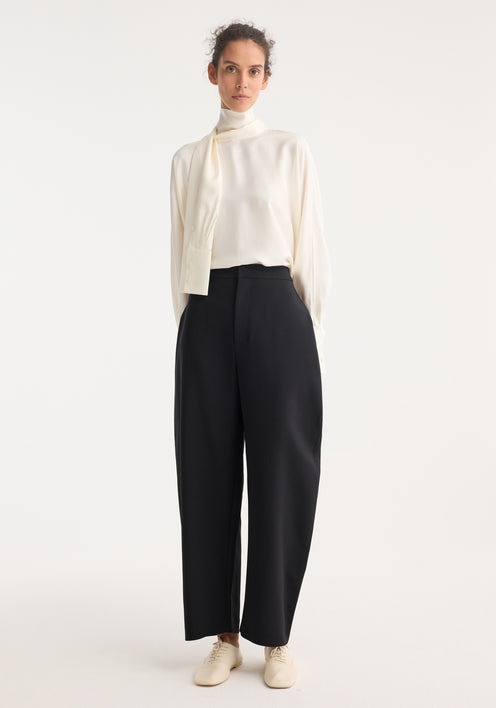 Model wearing Foulard silk top with draped sleeves, creating a scarf effect, paired with high-waisted black trousers and cream lace-up shoes.
