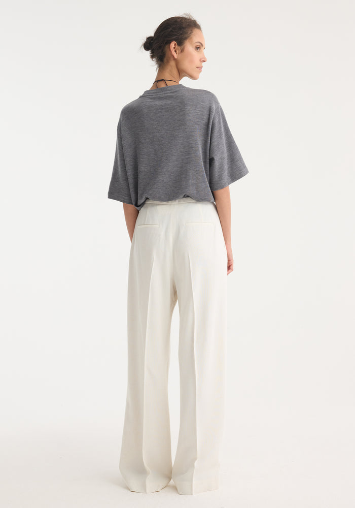 Person wearing relaxed drawstring trousers in winter white, showcasing a wide-leg fit and tucked charcoal-gray top, highlighting the trousers' elegant silhouette and fluid design.